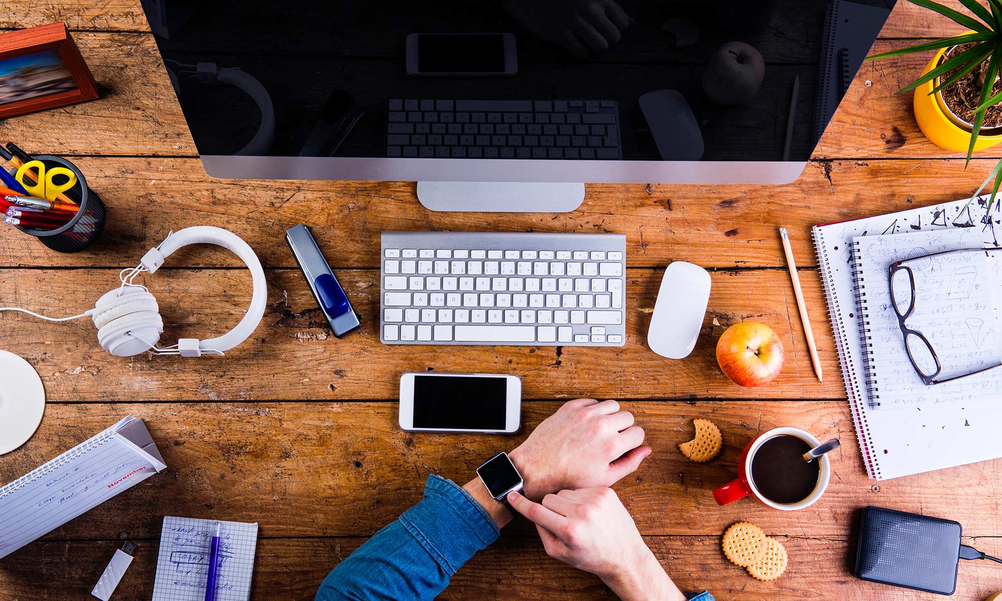 Desk with lots of gadget and man adjusting Apple Watch